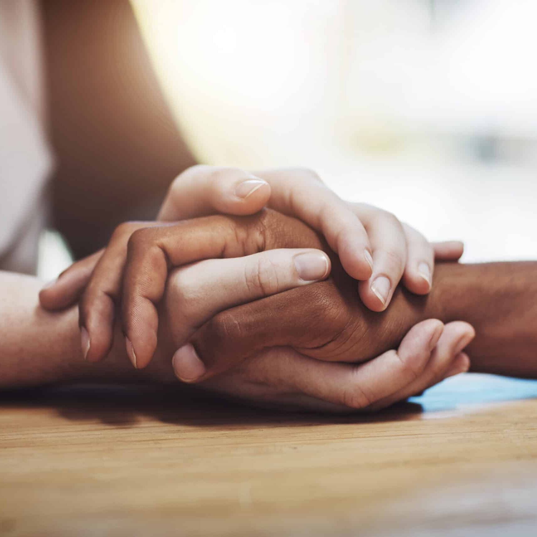Support, compassion and trust while holding hands and sitting together at a table. Closeup of a loving, caring and interracial couple or friends comforting each other after a loss or cancer news.