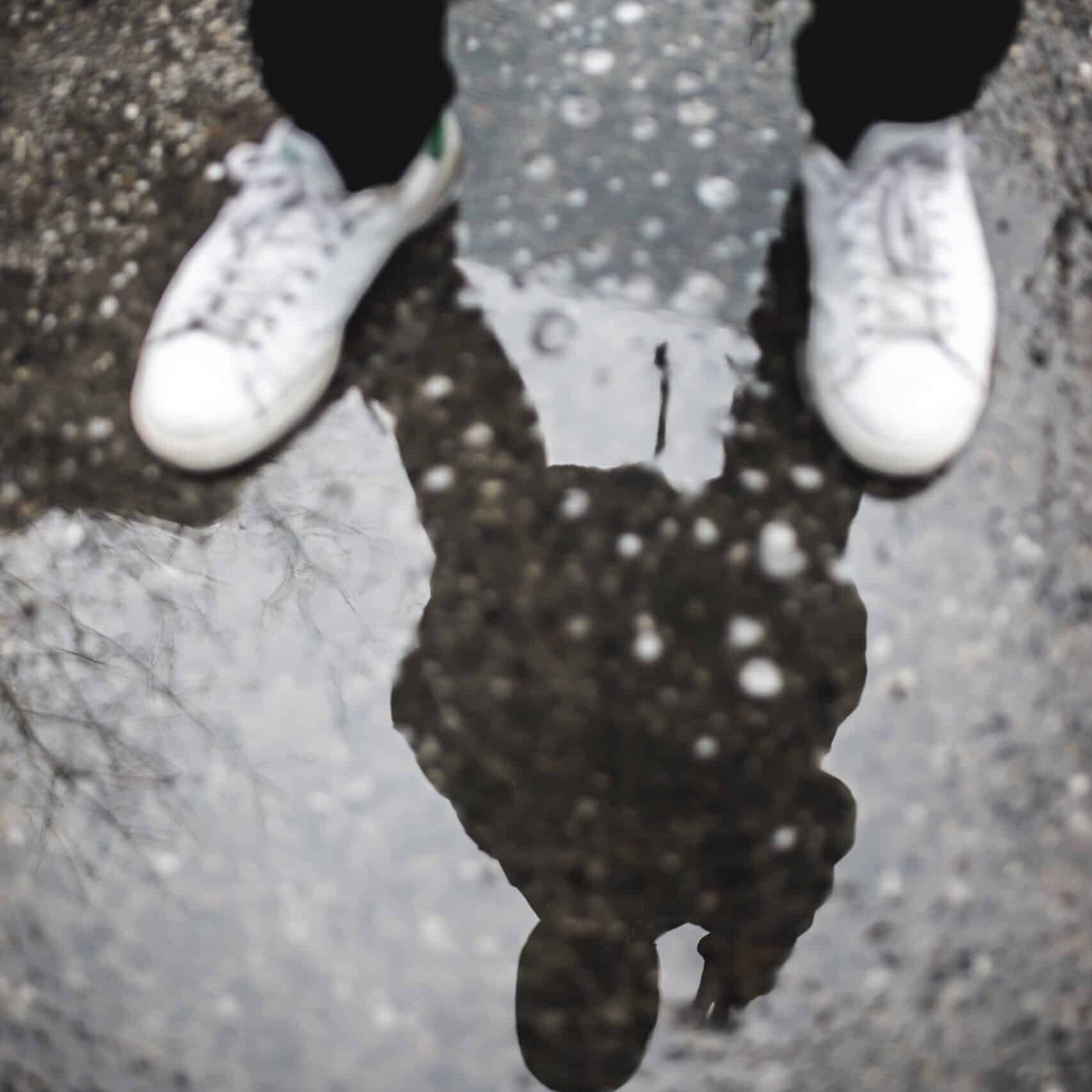 a person's reflection shows in a puddle